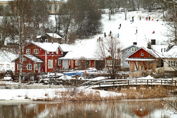 Local people are sledding at old historic Porvoo, Finland. Traditional Scandinavian rural red wooden houses and old river bridge under white snow. Snowing - 287442022