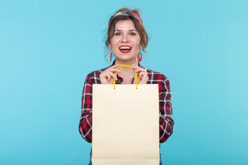 Happy young beautiful woman in a plaid shirt and jeans and holding a bag on a blue background....