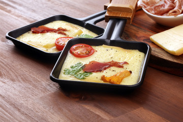 Delicious traditional Swiss melted raclette cheese on diced boiled or baked potato and baguette served in individual skillets with salami..
