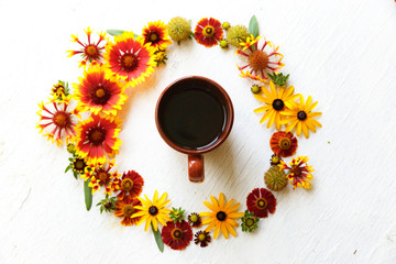 Cup of tea in middle of circle flower composition on a wooden white background