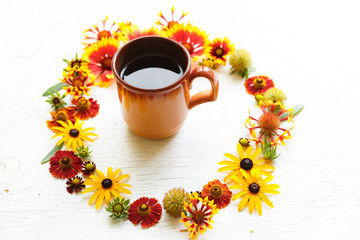 Cup of tea in middle of circle flower composition on a wooden white background