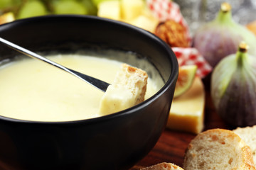 Gourmet Swiss fondue dinner on a winter evening with assorted cheeses on a board alongside a heated pot of cheese fondue with two forks dipping