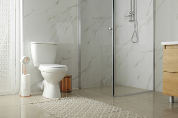 Toilet bowl near shower stall in modern bathroom interior