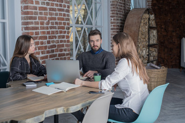 Group of successful internet worker discuss new ideas, sitting in co-working space with modern laptop computer. Three  intelligent freelancers create a new project for distance job, using net-book