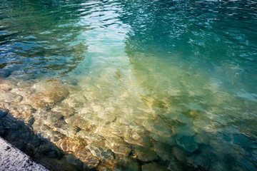 Lake or pond surface. Stone bed is seen through transparent water. Green and blue tints with sunlight flecks on it
