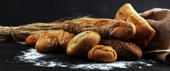 Assortment of baked bread and bread rolls on black table background