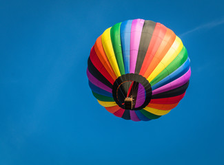 Rainbow colorful hot-air balloon floats on a summer morning with bright blue sky 