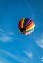 Fototapeta na wymiar Rainbow colorful hot-air balloon floats on a summer morning with bright blue sky 