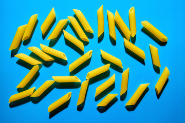 Yellow pasta on a blue background in hard light. Flat lay from macaroni