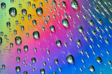 Water drops with reflection of the rainbow. Colorful abstract background. Blue, green, red and yellow abstract rainbow background. Closeup, selective focus