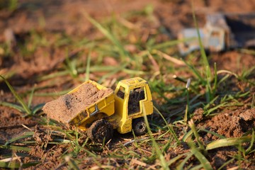 Close shot of a yellow toy truck on the ground near grass with a blurred background at daytime
