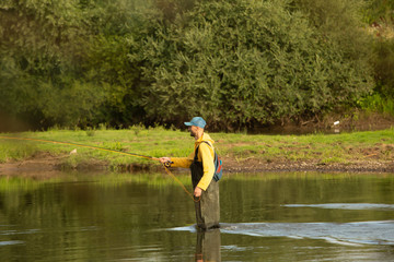 The fisherman stands at waist-deep in water. A man in a special waterproof suit throws a fishing rod