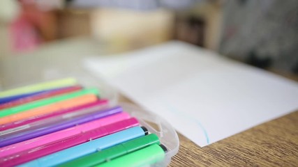 A girl puts a felt-tip pen in a box after drawing. The child puts the felt-tip pen in a box with multi-colored felt-tip pens. Children's drawing. Children draw in class at an educational institution.