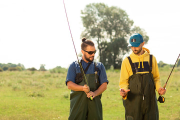 Two fishermen preparing for fishing. They hold the fishing rods and talk to each other. Sport fishing