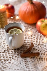 Fototapeta na wymiar Cup of warm tea with lemon with pumpkins, apples, candle and spices, fall scene