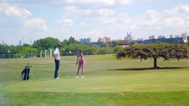 A girl hits a ball on a golf course while a man is watching.