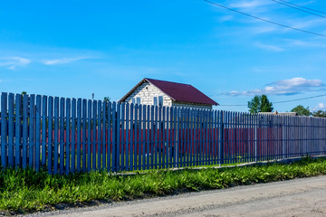 Low-rise not finished residential building and high fence in village in summer