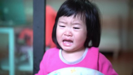 The little Asian girl very angry and upset, frowning her brow and showing a tongue. Bad mannered little girl  Crying in bed room