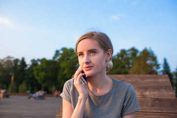 Fototapeta premium Carefree woman phoning via cellphone pda while sitting in city park during free time in vacation. Charming hipster girl having mobile phone conversation with boyfriend while relaxing outdoors
