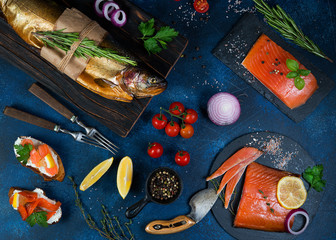 Set of different smoked fish on a concrete background. Trout, salmon and salmon on the table with spices and vegetables. Top view