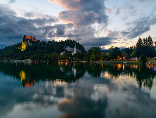 Fototapeta na wymiar Evening (blue hour) landscape on Lake Bled with reflection and beautiful cloudy sky.