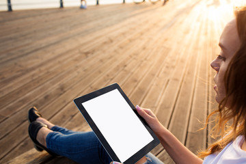Hipster woman holding portable touch pad with empty copy space screen background for promotional content while relaxing outdoors on embankment river in sunny summer day. Female using digital tablet