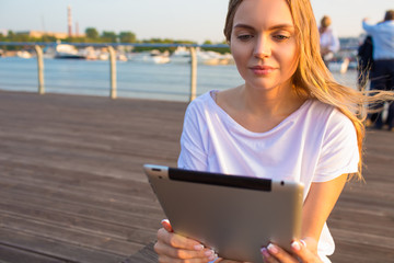 Young beautiful woman online shopping store via portable touch pad while relaxing on embankment river near copy space for promotional content. Hipster girl chatting via digital gadget during rest