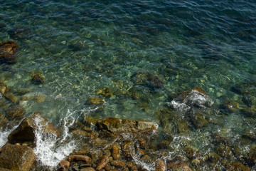 Top view on the sea near coast with waves and crystal clear water. Waves broken by rocks. Horizontal line
