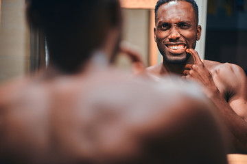 Handsome african man is checking his teeth in the bathroom while see himself in the mirror.