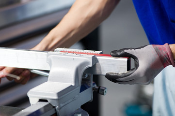 master in a blue T-shirt and gray gloves clamps a part in a vice, a worker at a workbench, close-up