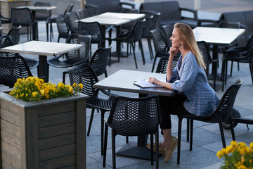 Attractive blond businesswoman is thinking about her job while sitting at cafeteria's outside with paperworks.