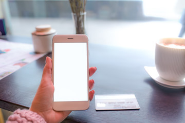 Closely woman lifestyle blogger holding smartphone with white empty mock up on the screen background for promotional content during online payment and using credit card, sitting in coffee shop
