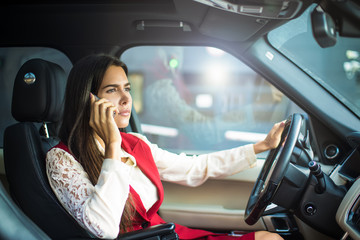 Confident prosperous business woman in formal wear having serious mobile phone conversation while driving a luxury car. Proud female owner phoning via cell telephone, sitting in modern automobile