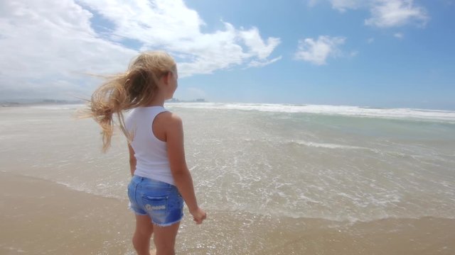 Girl looking at sea with wind in her hair. Beautiful blond hair develops in the wind and she is happy. Child by the sea with waves.