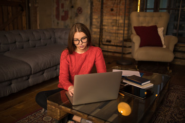 Young hipster girl smart blog writer typing article on web page via pc laptop computer, sitting at coffee table in home interior. Female university student having online learning via netbook gadget