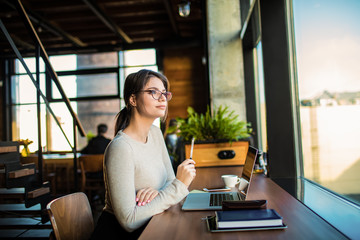 Thoughtful woman professional writer thinking while sitting with laptop computer in coworking space 