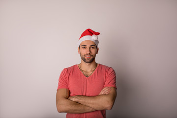 Portrait of a handsome caucasian man in stylish shirt and red Canta Clause hat posing for camera while standing with crossed arms isolated in studio against grey background with copy space