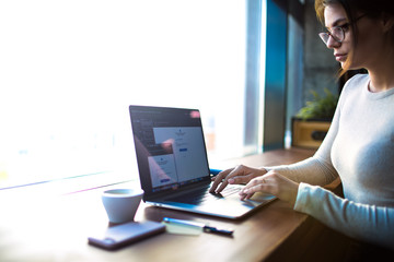 Hipster girl in spectacles professional marketing coordinator working on portable pc laptop...