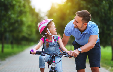 happy family father teaches child daughter to ride a bike in the Park  .