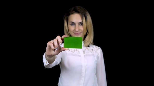 Young businesswoman in a white shirt holds a bank card in her hand. Isolated black background. Chromakey green card. 4k