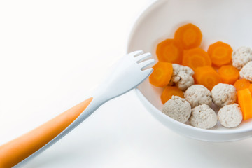 Food for kids, first lure for babies, pieces of carrot and turkey in a plate on a white background.