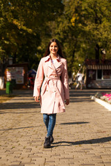 Portrait of a young brunette girl in pink coat on a background of autumn park