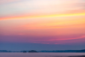 Naklejka na ściany i meble Morning before sunrise. A multicolored sky and a sea of mist beneath it.