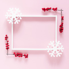 Christmas modern composition. Xmas decorations, photo frame, red berries, snowflakes on pastel pink background. Christmas, New Year, winter concept. Flat lay, top view, copy space, square