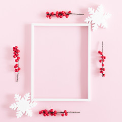 Christmas modern composition. Xmas decorations, photo frame, red berries, snowflakes on pastel pink background. Christmas, New Year, winter concept. Flat lay, top view, copy space, square