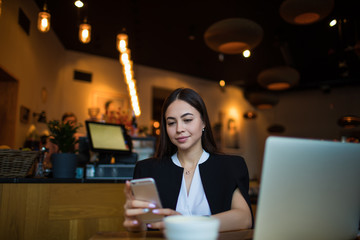 Attractive woman real estate analyst reading e-mail on mobil phone while sitting in restaurant during coffee break. Female leadership browsing wifi on smartphone gadget, resting in cafe during leisure