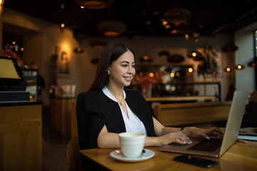 Happy smiling business woman having online conference via laptop computer, sitting in restaurant. Cheerful female employer having video call via notebook. Webinar via netbook gadget