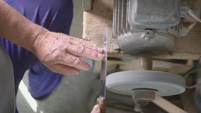 Adult specialist sharpening steel knife on wheel lathe. Man grinding on abrasive cutting and knife-sharpening stones. Knife care and maintenance concept.
