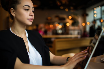 Successful business woman searching resume on site via touch pad computer, sitting in restaurant. Serious confident female checking e-mail on digital gadget, resting in coffee shop. Online booking