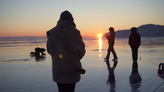 Tourists on frozen Lake Baikal against orange sky during sunset